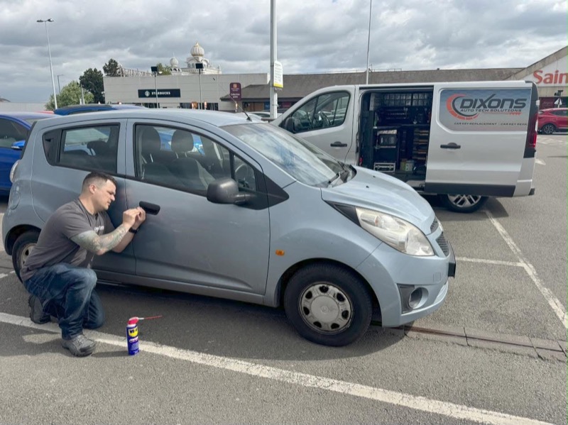 Working on a customer's car door in a car park, with the Dixon's van parked behind
